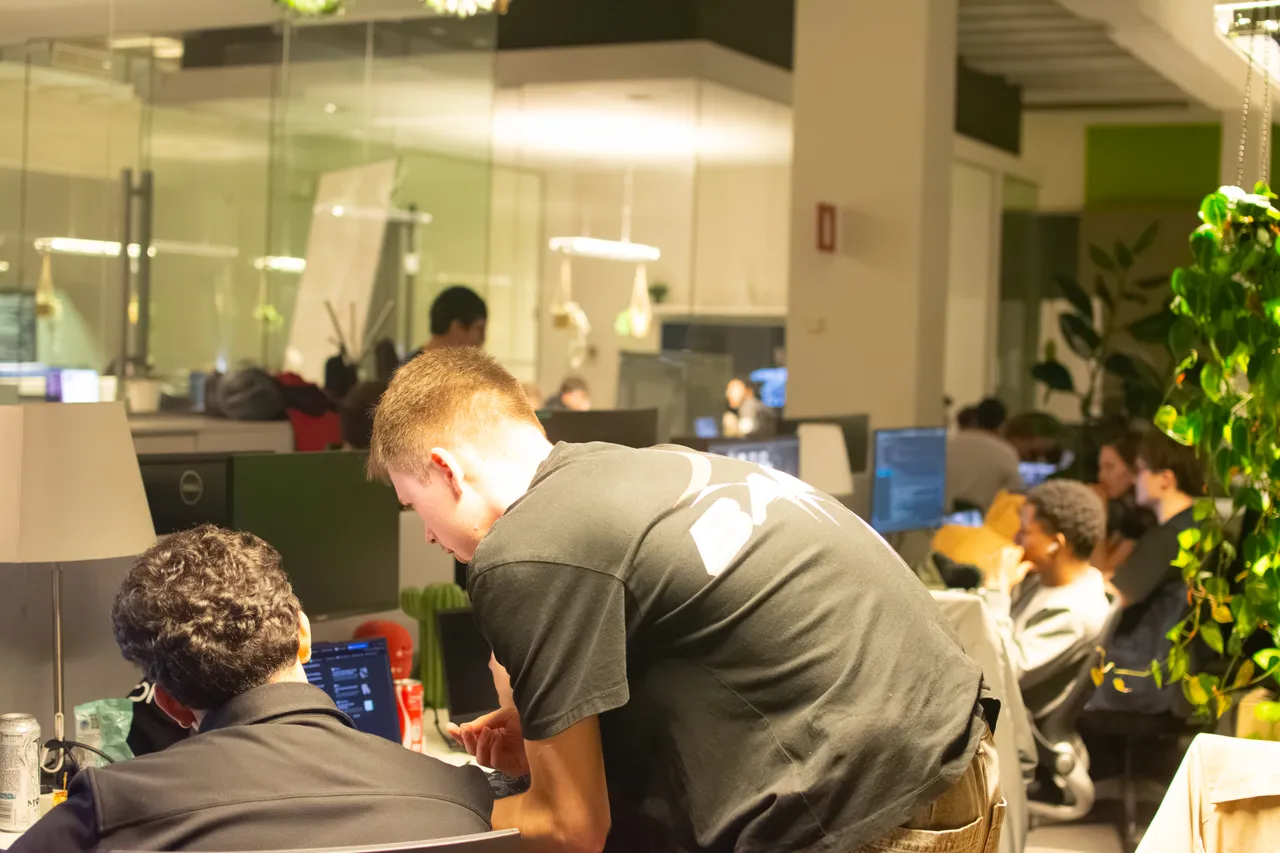 Hackathon participants working together at laptops with support from an organizer.
